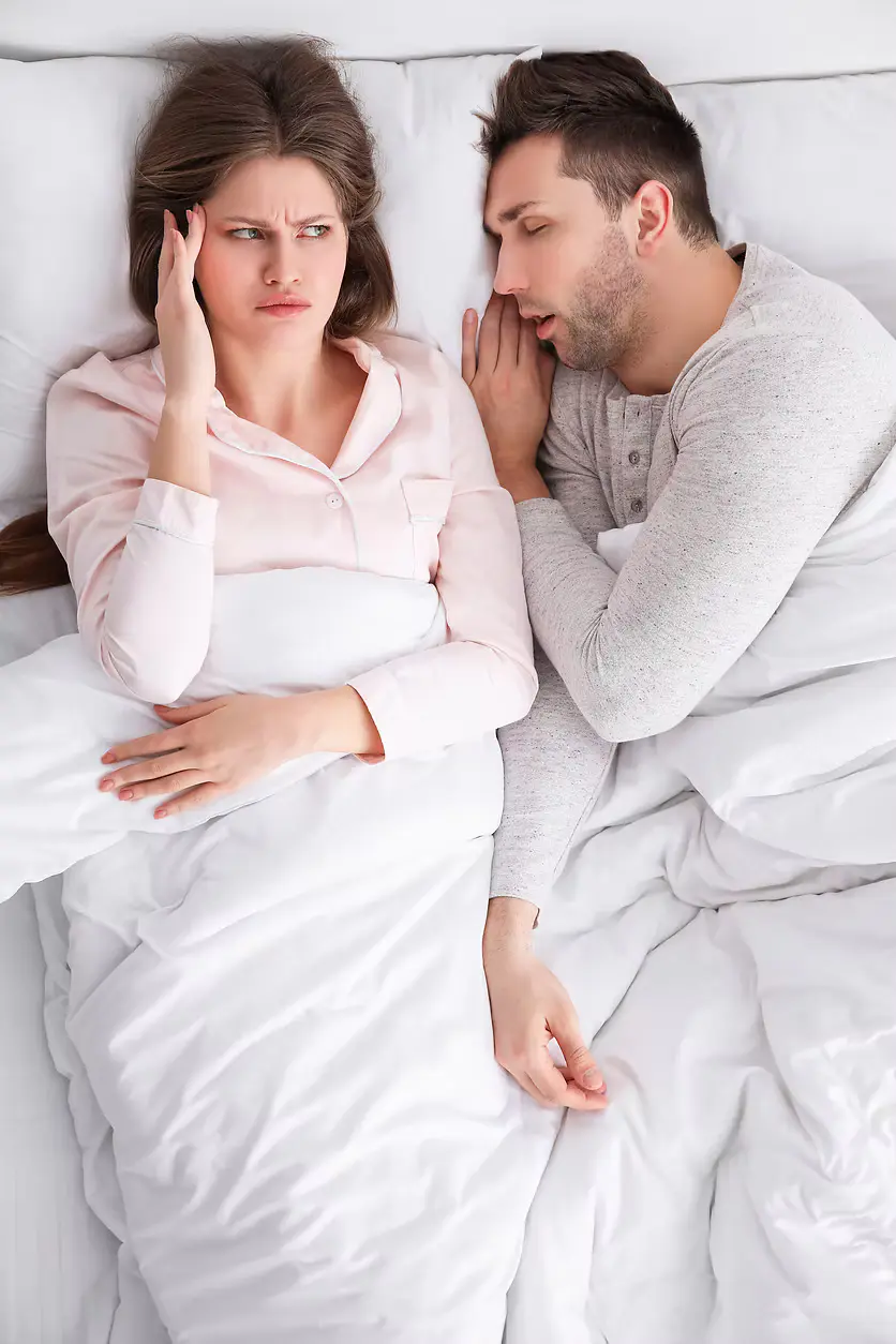 An upset woman sleeping next to snoring man in bed